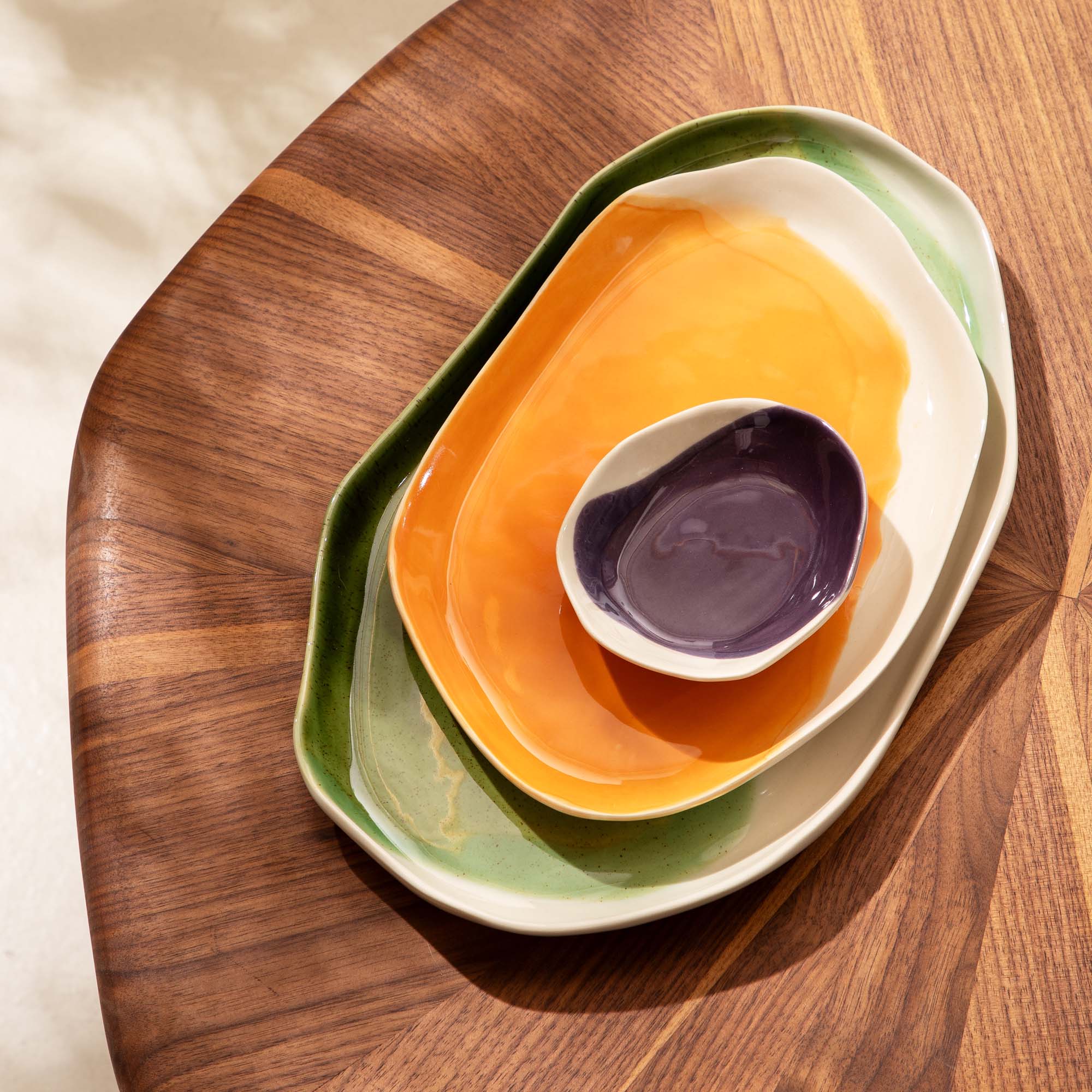 3-piece serving tray set nested in green, orange and aubergine glazes on a walnut table