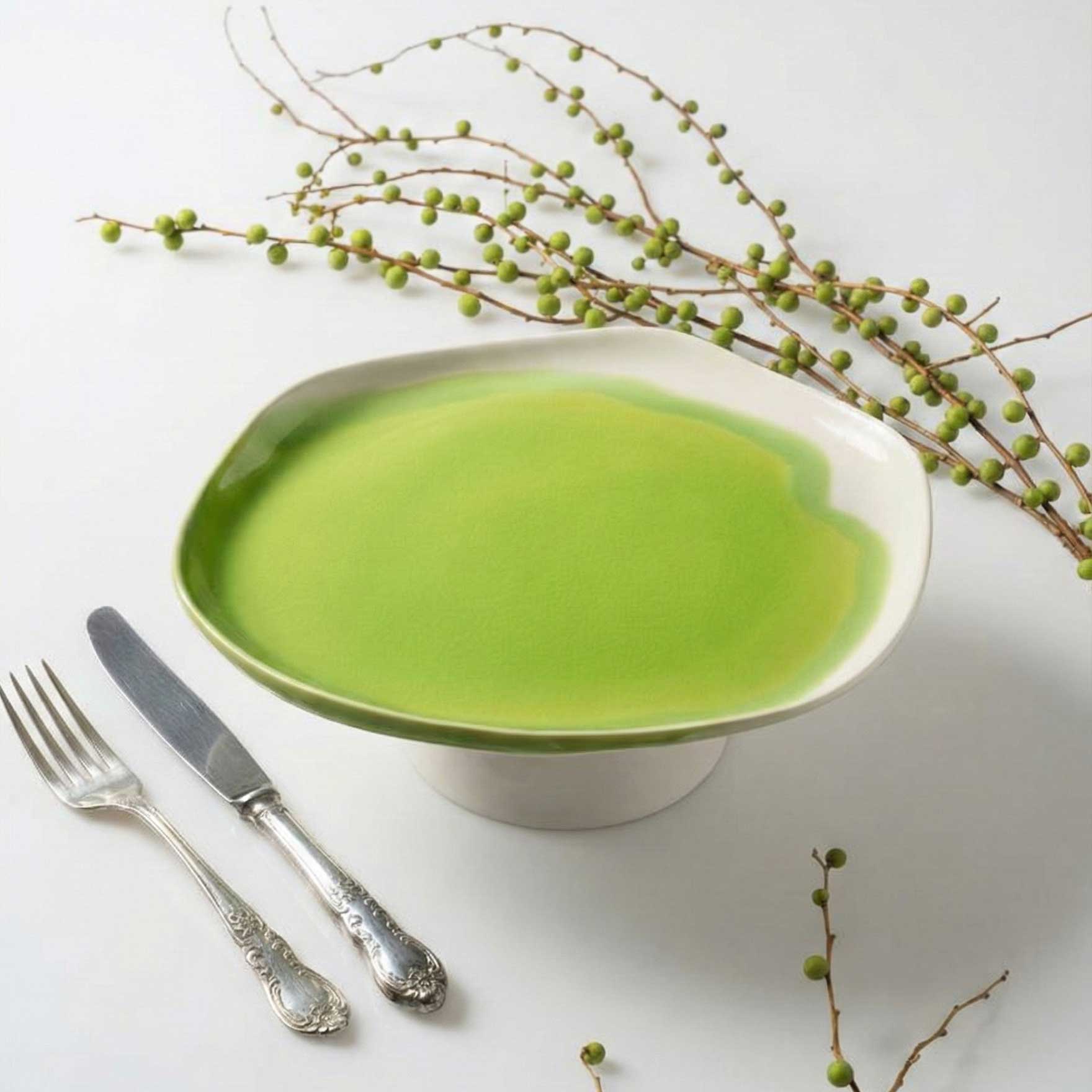 Artistic cake stand in lime green glaze with antique cutlery and budding branches