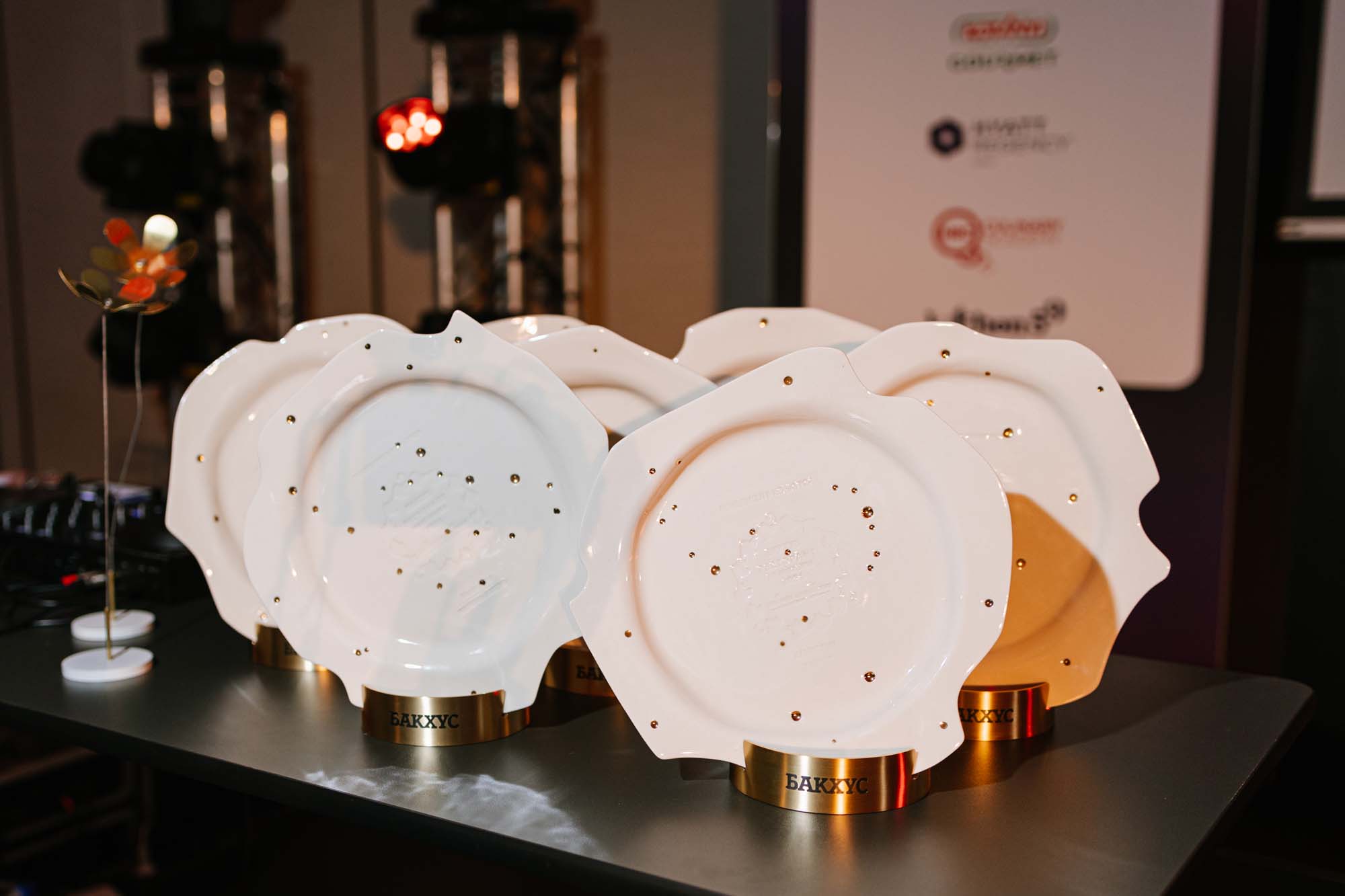 Row of Bacchus Restaurant of the Year award plates in white porcelain standing on a stage table
