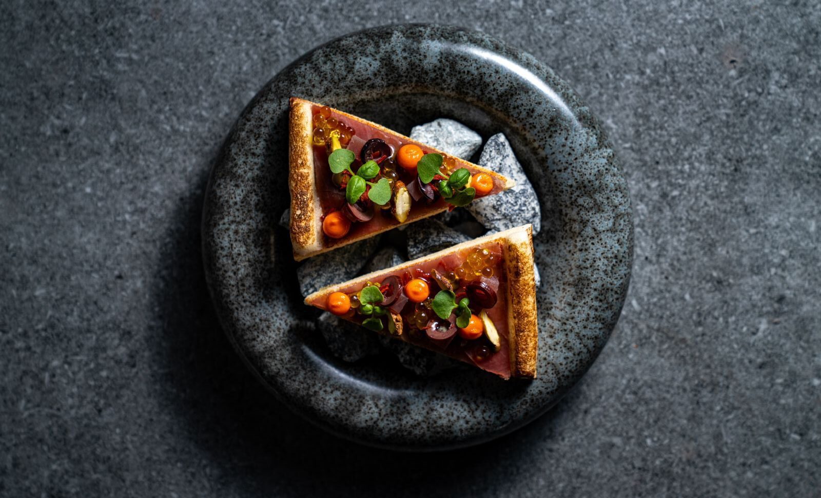 Custom restaurant plate in dark speckled glaze with two slices of vegetable tart, fine dining