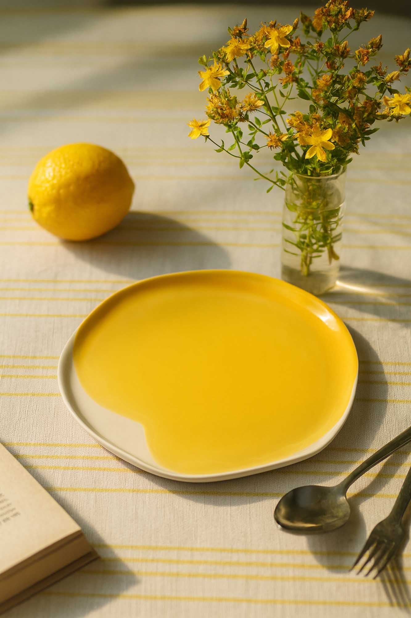 Handmade porcelain plate in Cadmium Yellow glaze on a striped linen with lemon and wildflowers