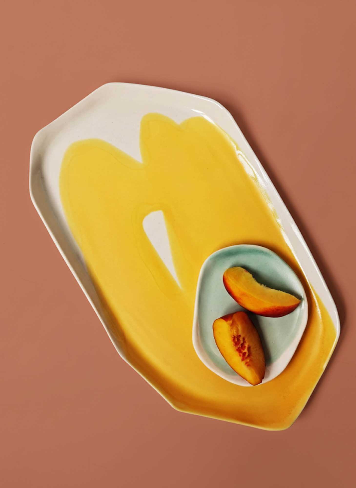 Cadmium Yellow porcelain platter with a small mint bowl of sliced peaches on terracotta background