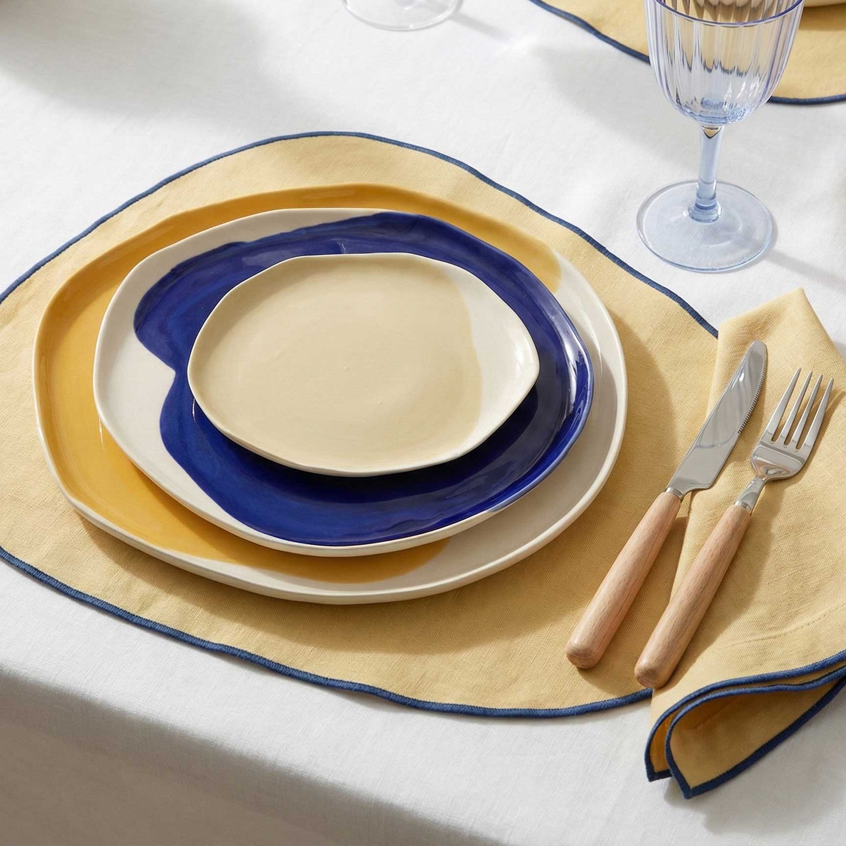 FW 2026 table setting with ivory and Dark Denim rimmed porcelain plates on a yellow placemat