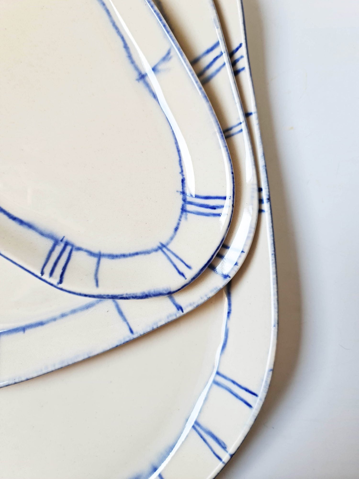 Stacked ivory porcelain platters with hand-painted Royal Blue brushstroke rims, close-up