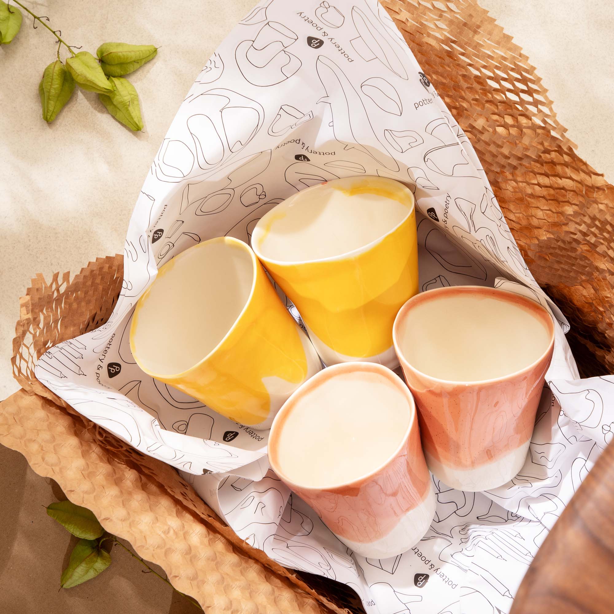 Set of 4 handmade porcelain cups in yellow and peach glaze nestled in patterned paper