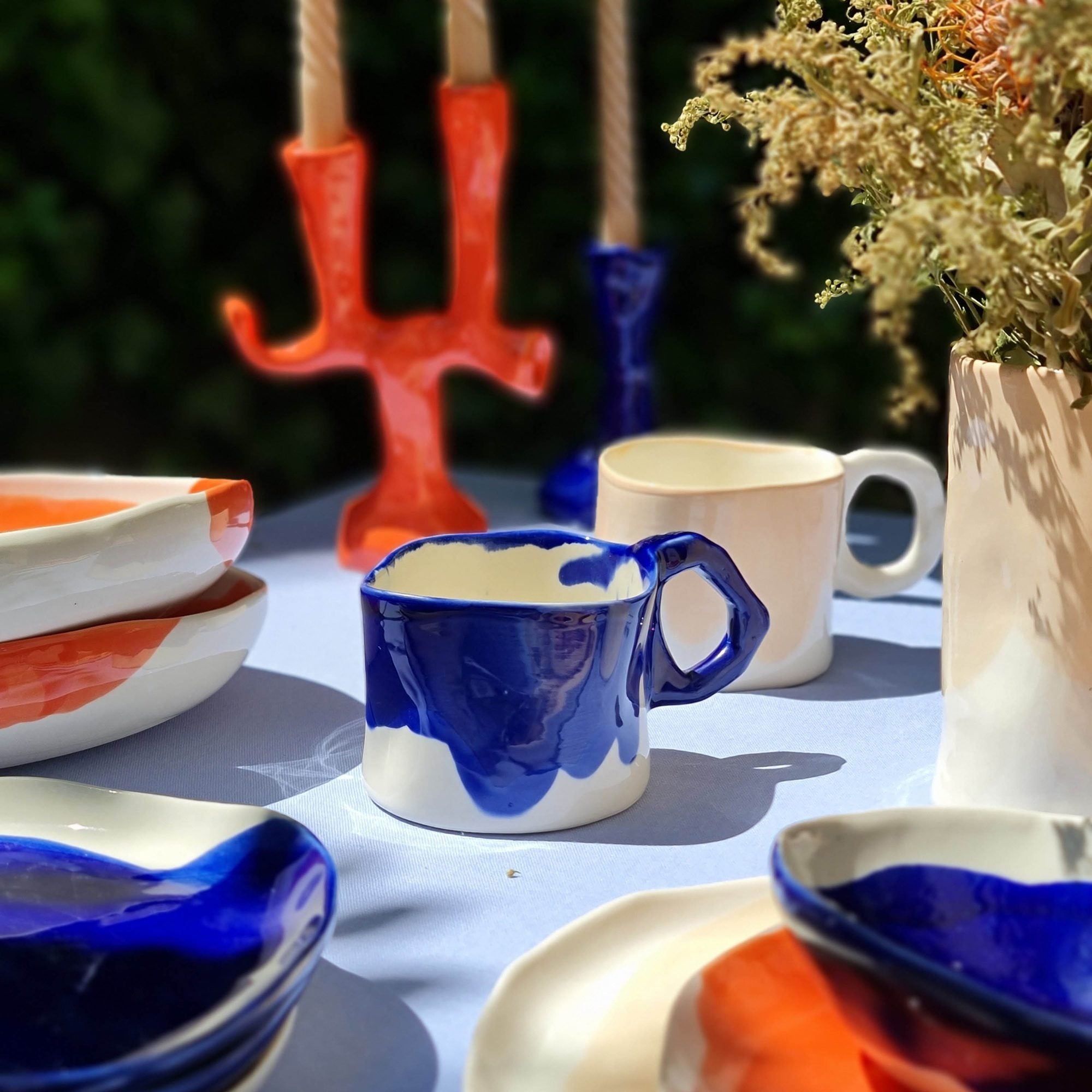 Set of four handmade ceramic mugs with cobalt blue glaze splashes on an outdoor summer table