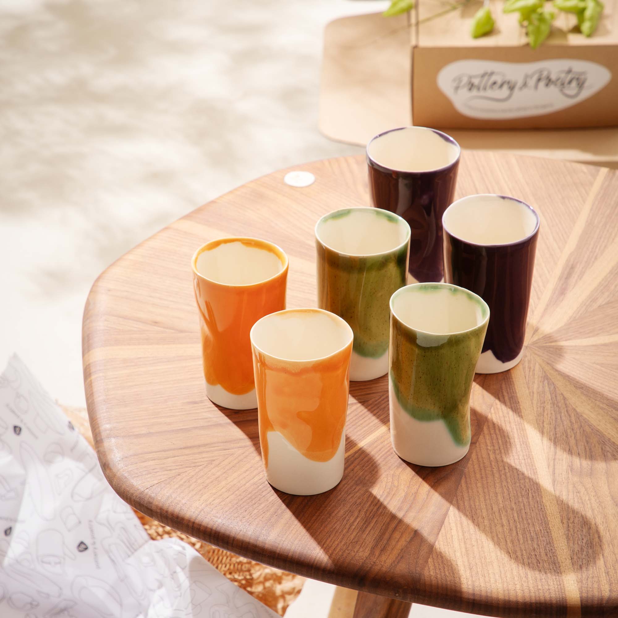 Set of 6 handmade porcelain tumblers in orange, olive green and aubergine glazes on a wooden table