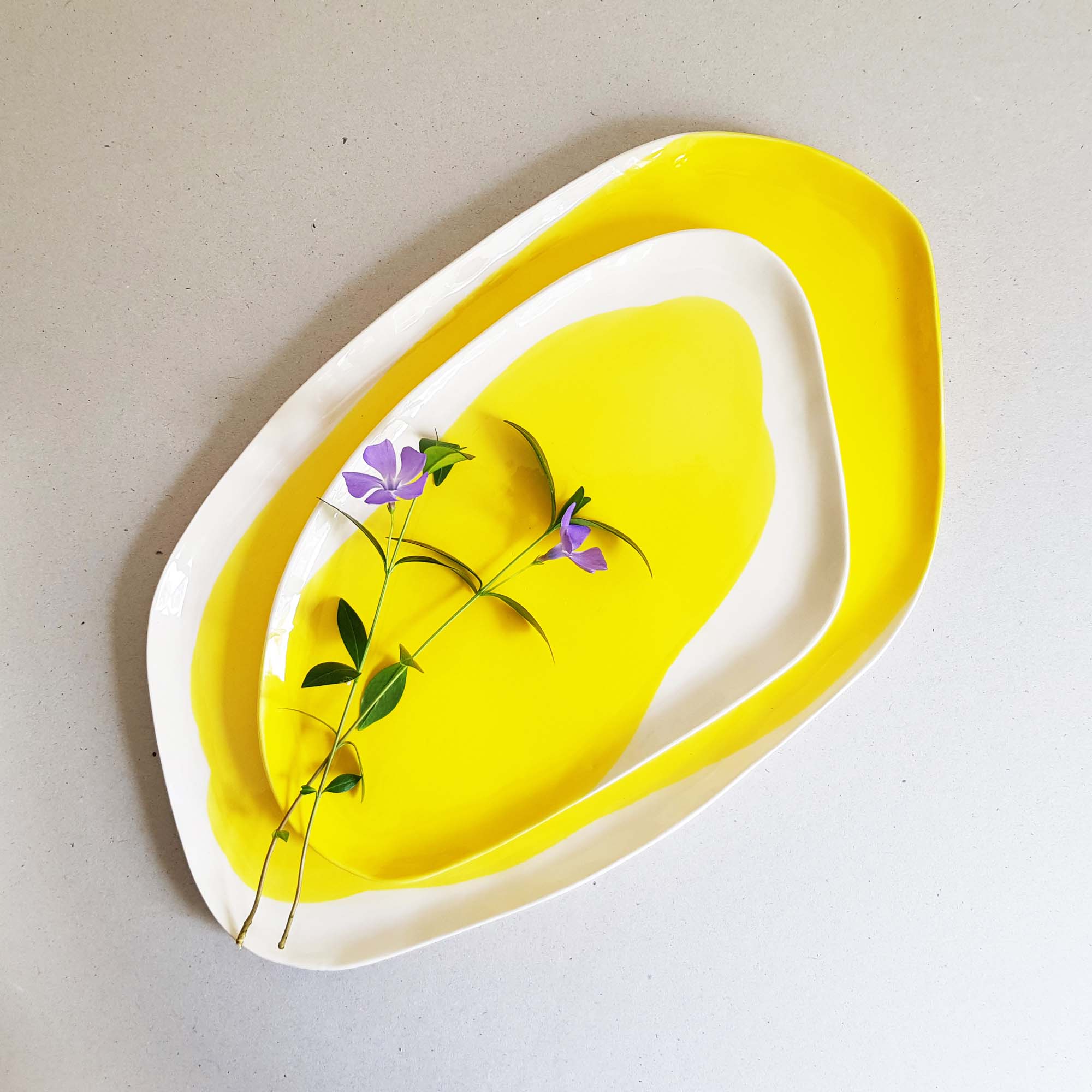 Nested serving trays in Lemon Yellow glaze with white edges, styled with a sprig of violet flowers