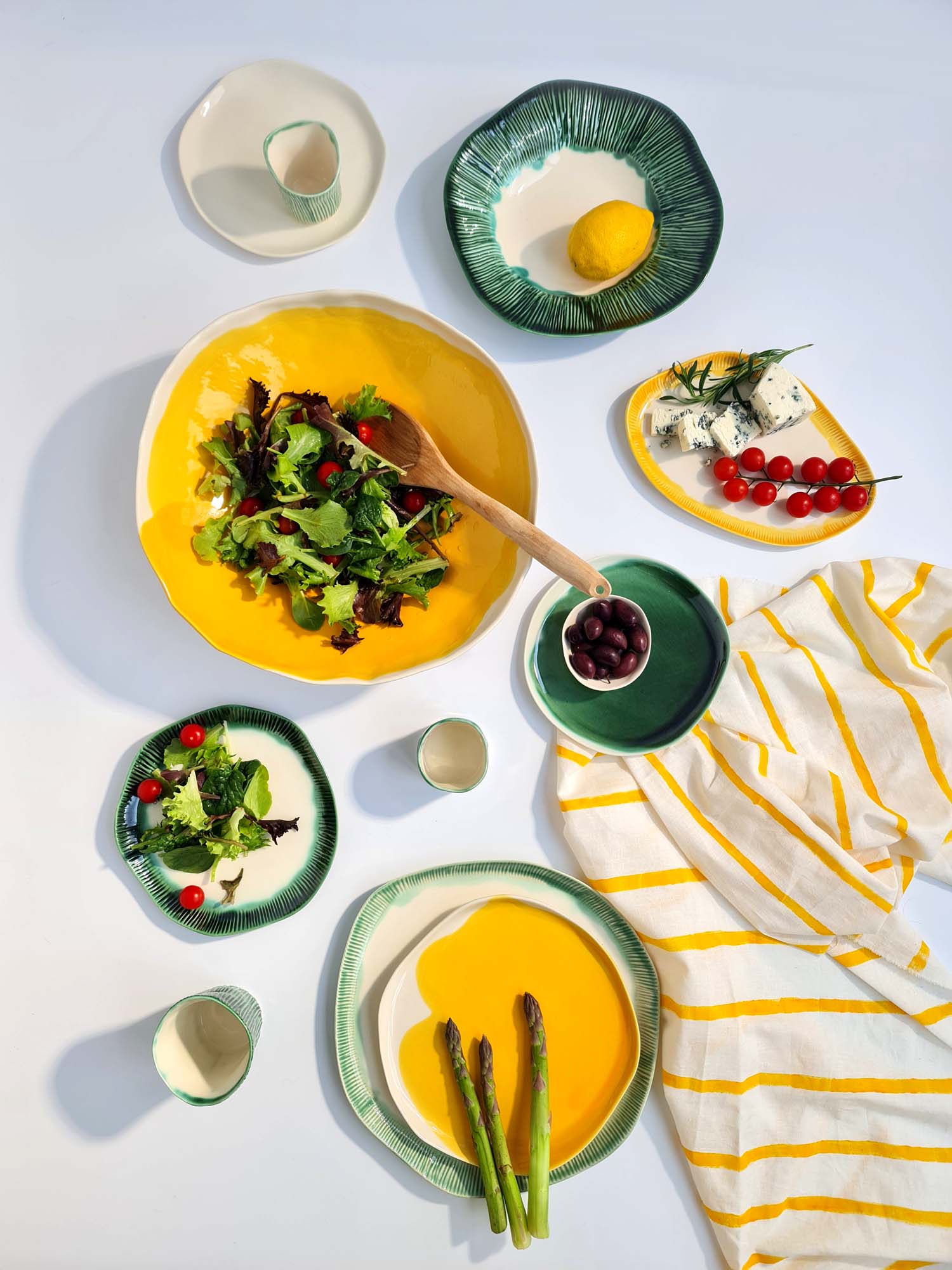 Summer table of yellow and green handmade porcelain plates with salad, asparagus and tomatoes