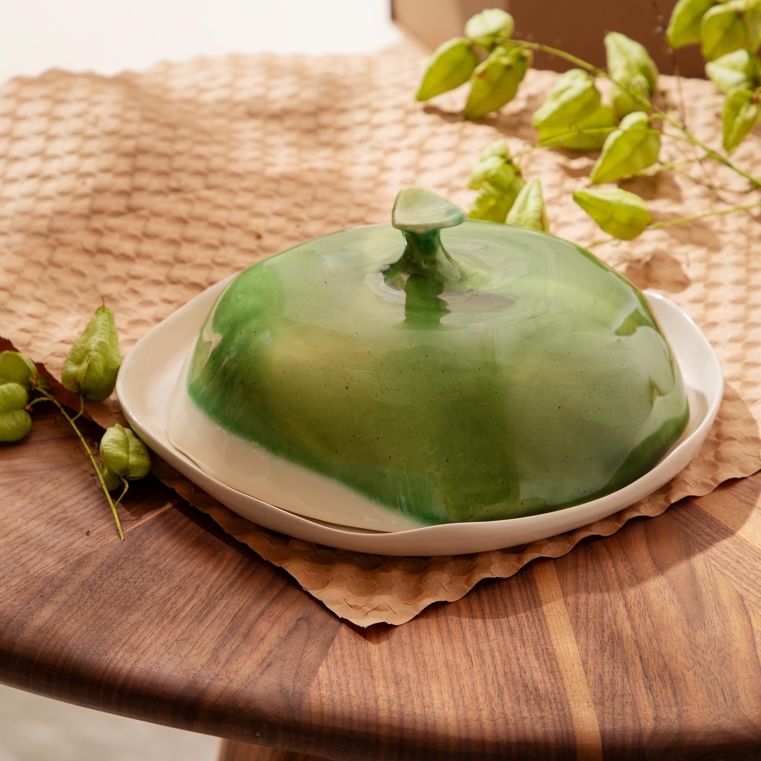 Handmade porcelain butter dish in green glaze on a wooden board with vine leaves